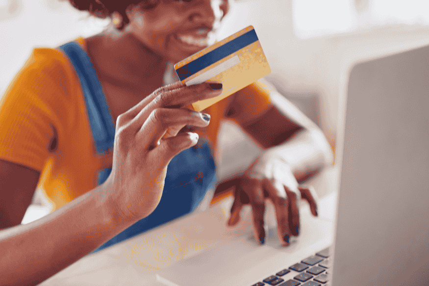 Smiling woman holding a credit card while shopping online on her laptop