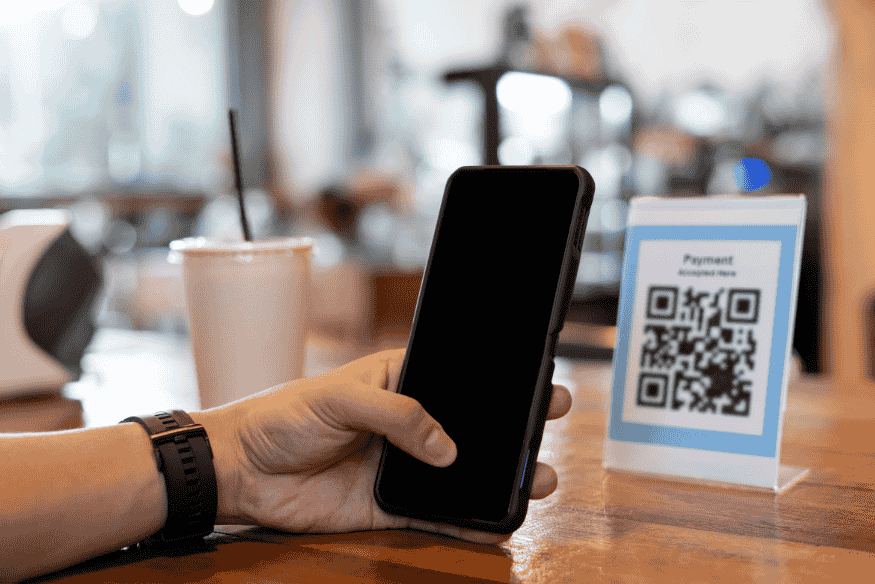 Customer using a smartphone to scan a QR code for digital payment at a café.