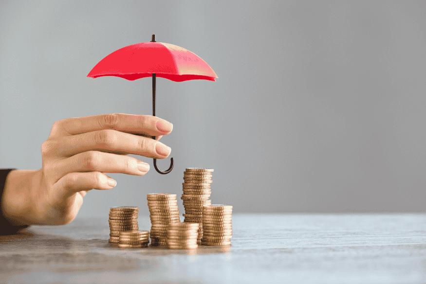 Hand holding a red umbrella over stacked coins symbolizing financial protection.