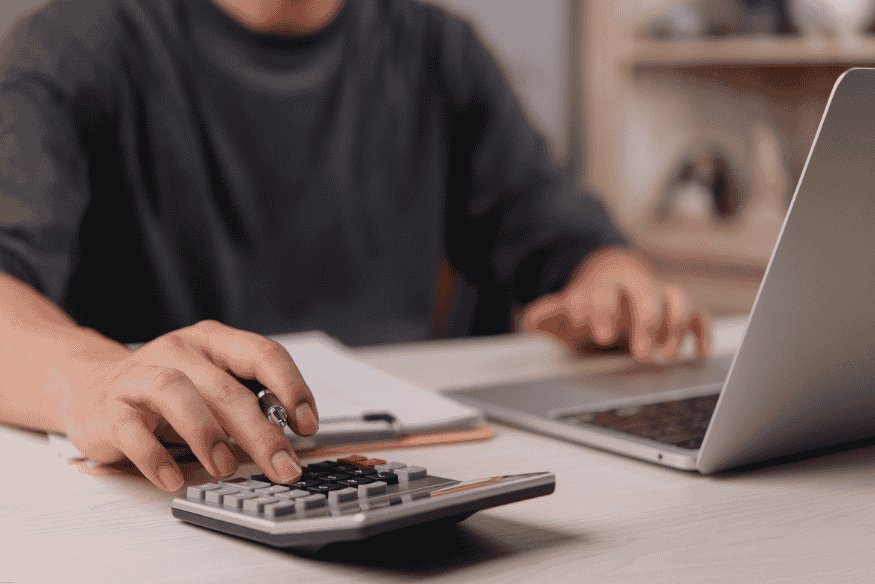 Freelancer using a calculator and laptop to manage taxes and expenses.