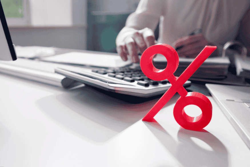 Red percentage symbol in front of a person calculating taxes at a desk.