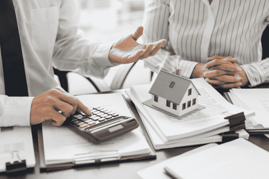 Business professionals discussing property investment with model house and calculator