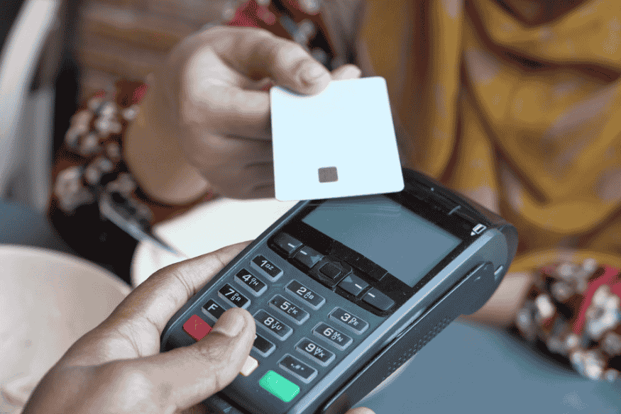 Person making a contactless payment with a white credit card on a POS terminal