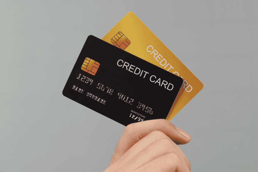 Hand holding two credit cards, one black and one gold, against a neutral background