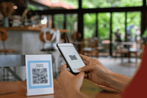 Person scanning a QR code on a table sign using a mobile payment app.