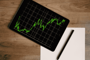 Tablet showing upward stock chart on wooden desk with pen and paper