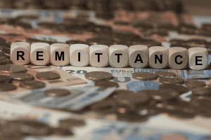 Word “Remittance” spelled with letter cubes on top of various coins and banknotes.