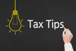 Hand writing “Tax Tips” on a blackboard with a yellow lightbulb illustration.